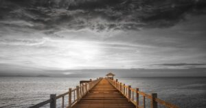 Wooden pier with railings extending straight toward the horizon over calm water at sunset, with dramatic sky above, representing the clear path forward from engagement to conversion]