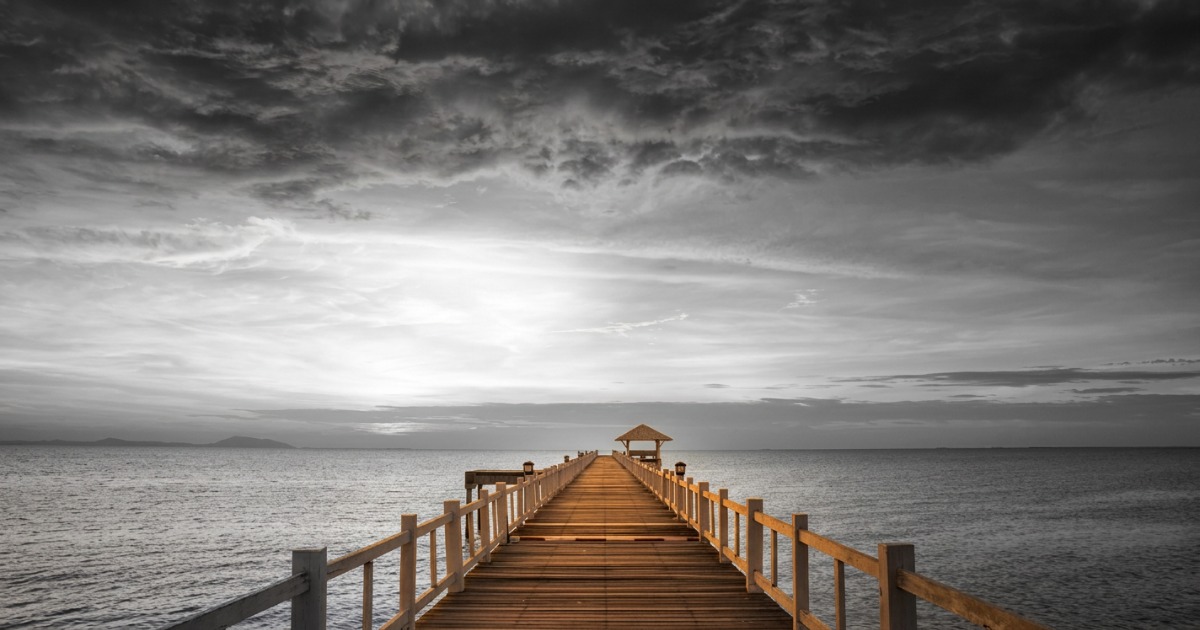 Wooden pier with railings extending straight toward the horizon over calm water at sunset, with dramatic sky above, representing the clear path forward from engagement to conversion]
