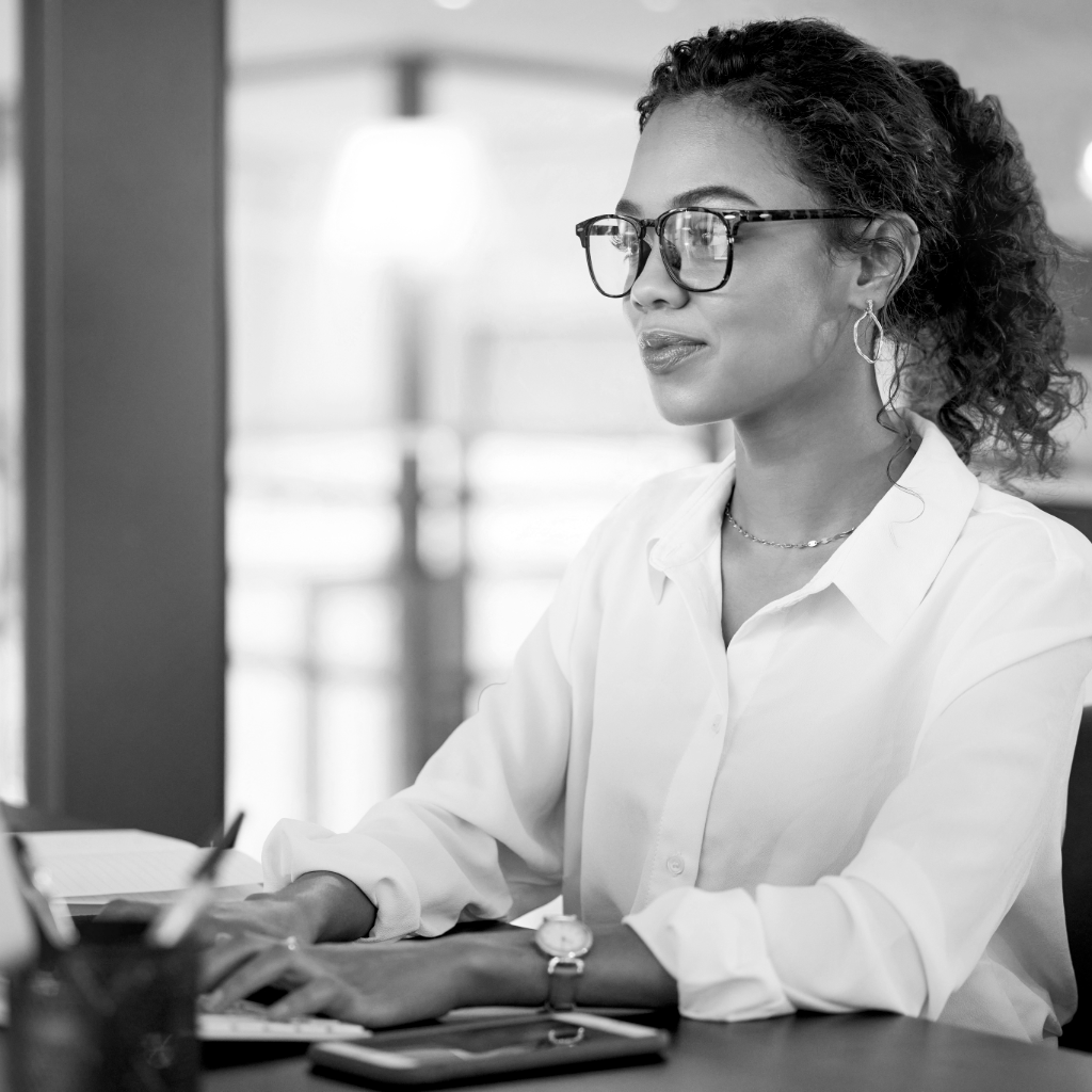 A women working at a computer with black glasses and a white shirt.
